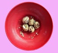 five quail eggs, one of which was half peeled in a red bowl, isolated on pink Royalty Free Stock Photo