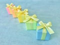 Five rainbow gradient colors square gift boxes arranged in a diagonal row on a blue-green watercolor textured background. Royalty Free Stock Photo