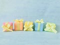 Five rainbow gradient colors square gift boxes randomly arranged in a row on a blue-green watercolor textured background. Royalty Free Stock Photo