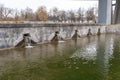Flowing water from several rectangular spouts enters a green water basin near a bridge during winter day Royalty Free Stock Photo