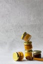 Five Small glass jar with metal cap with different kinds and colours of honey one on another and spoon isolate and on grey cement