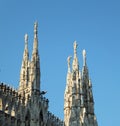 Five of the spires of the Duomo di Milano standing in groups of three and two, tall against blue summer sky