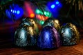 Five sweets wrapped in foil lie on a wooden surface. Background - Christmas tree and multi-colored LED lights. Night magic. Bokeh Royalty Free Stock Photo
