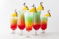 Five tall colourful mocktails garnished with pineapple wedges against a light background.