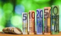 Five, ten, twenty, fifty and one hundred euro rolled bills banknotes, with euro coins on green blurred bokeh background. Royalty Free Stock Photo