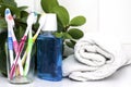 Five toothbrushes in a glass cup mouthwash and a rolled up towel on the dressing table against the green foliage