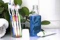 Five toothbrushes in a glass cup mouthwash a tube of toothpaste and a rolled up towel on the dressing table against a backdrop of