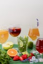 Five tropical mixed drinks, orange, lemon and raspberries cocktails over bright pastel green background.