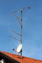 Five TV antennas next to one satellite dish mounted on single metal pole on top of new family house roof