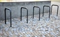 Five wheel stands of black metal bent tube in the shape of a rectangle in front of the retaining wall paving of granite cubes in Royalty Free Stock Photo