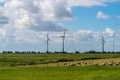 Five wind turbines for energy generation in green meadows, sheep graze in front of it. Blue sky with white clouds. Near Pilsum