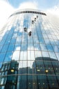 Five window washers work at a height on a high-rise building with a glazed facade against a blue sky with light clouds