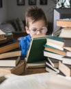 Five year old boy in glasses reading a book with a stack of books next to him Royalty Free Stock Photo