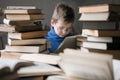 Five year old boy in glasses reading a book with a stack of books next to him Royalty Free Stock Photo