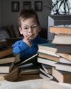 Five year old boy in glasses reading a book with a stack of books next to him. Smart intelligent preschool kid choosing books to Royalty Free Stock Photo