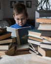 Five year old boy in glasses reading a book with a stack of books next to him. Smart intelligent preschool kid choosing books to Royalty Free Stock Photo