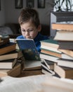 Five year old boy in glasses reading a book with a stack of books next to him. Smart intelligent preschool kid choosing books to Royalty Free Stock Photo