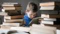 Five year old boy in glasses reading a book with a stack of books next to him. Smart intelligent preschool kid choosing books to Royalty Free Stock Photo