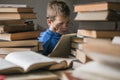 Five year old boy in glasses reading a book with a stack of books next to him. Smart intelligent preschool kid choosing books to Royalty Free Stock Photo