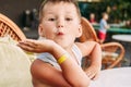 Five-year-old Caucasian boy grimaces at a table in a summer cafe. Children and summer holidays. Hotel bracelet on hand