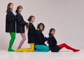 Five young beautiful different women in black jackets and colored tights sitting on floor and looking at camera with