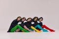 Five young beautiful different women in black jackets and colored tights sitting on floor and looking at camera with