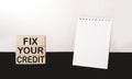 Fix Your Credit text written on building blocks and white and black background, next to a notepad for writing.Conceptual photo. Royalty Free Stock Photo