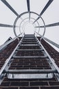 Fixed ladder going up the side of a brick building fitted with a steel safety cage