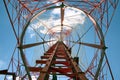 A fixed ladder or maintenance ladder for going to the top of a self-supporting telephone tower against blue sky and clouds