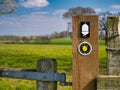 Fixed to a wooden post on a stile, a direction marker and white acorn logo of a Natural England National Trail Royalty Free Stock Photo