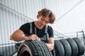 Fixes broken tire. Adult man in grey colored uniform works in the automobile salon