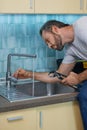 Fixing leaky faucet. Professional plumber looking concentrated, using pipe wrench while examining and fixing faucet in