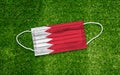 Flag Bahrain placed on a medical mask lies on the green grass. Covid-19 pandemic concept
