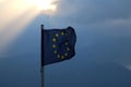 The flag of the european union flies in the wind against a dark sky from which the sun`s rays break through Royalty Free Stock Photo