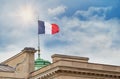 Flag of France is on the top of the roof of parisian building. Blue sky, clouds and sun on the background.