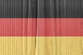 Flag of Germany on dry pale wooden surface. German national symbol. Hard sunlight with shadows on old wood. Faded vintage