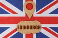 On the flag of Great Britain lies a symbol of geolocation and cardboard with the inscription - Edinburgh