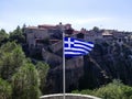 Flag of Greece is displayed against background of ancient monastery located on impregnable rock.