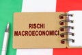 On the flag of Italy lies a pen and a notebook with the inscription - macroeconomic risks