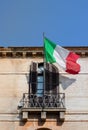 Flag of Italy waving on a balcony of classical Roman building with blue sky