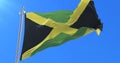 Flag of Jamaica waving at wind with blue sky in slow, loop
