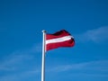 The flag of Latvia in the wind with blue cloudy sky. Exact colours of Latvian flag - carmine red with white horizontal stripe. The