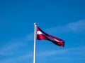 The flag of Latvia in the wind with blue cloudy sky. Colours of Latvian flag - carmine red with white horizontal stripe