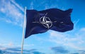 Flag of NATO waving in the wind on flagpole against the sky with clouds on sunny day