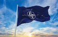 Flag of NATO waving in the wind on flagpole against the sky with clouds on sunny day