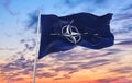 Flag of NATO waving in the wind on flagpole against the sky with clouds on sunny day