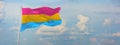 flag of Pansexuality Pride waving in the wind on flagpole against the sky with clouds on sunny day. panoramic view with copy space