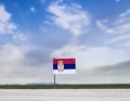 Flag of Serbia with vast meadow and blue sky behind it.