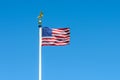 The flag of the United States of America blowing in the wind on a white pole against blue sky