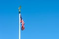 The flag of the United States of America dangling on a white pole against blue sky